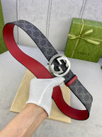 Gucci belt held up: dark monogram strap with red lining, silver circular GG buckle.