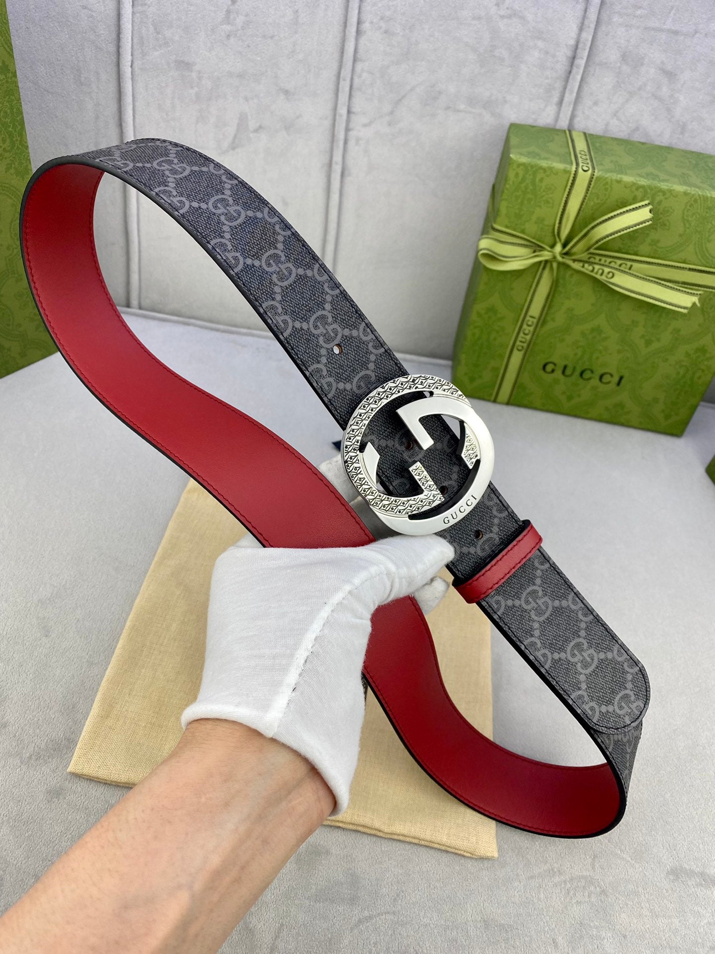 Gucci belt held up: dark monogram strap with red lining, silver circular GG buckle.