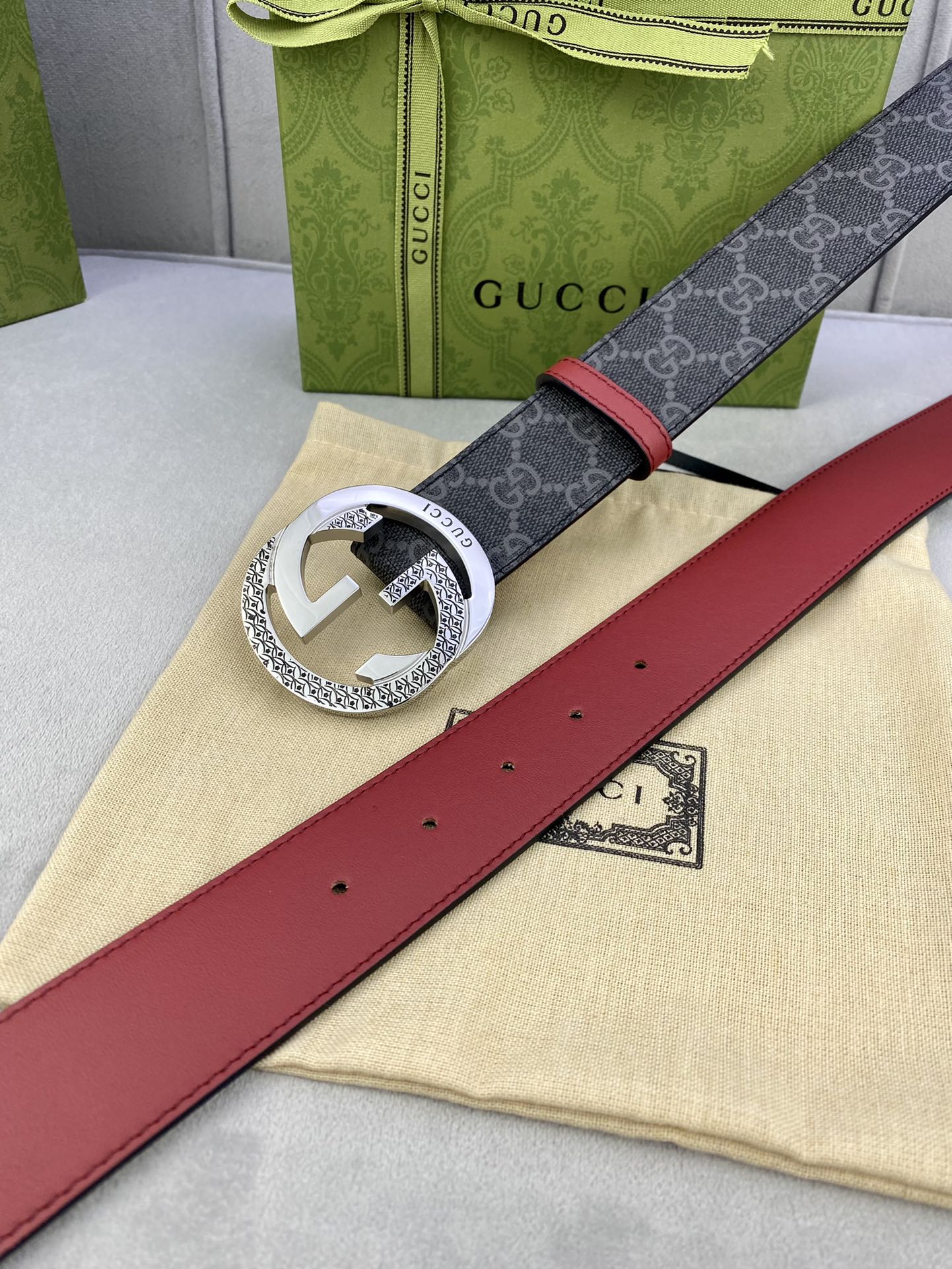 Gucci belt laid flat: dark monogram strap, red leather center, silver buckle with holes.