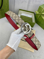 Gucci belt held in white-gloved hand, beige GG canvas with red leather strap