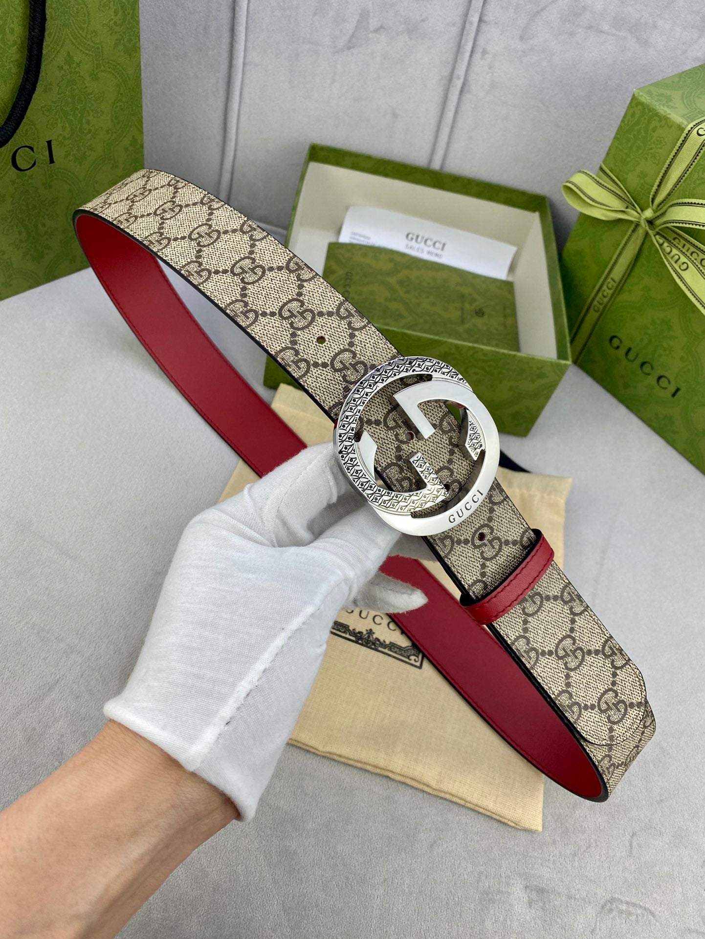 Gucci belt held in white-gloved hand, beige GG canvas with red leather strap