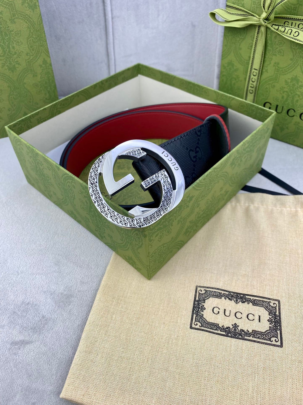 Gucci belt in green box with dark monogram strap, red trim, and silver buckle
