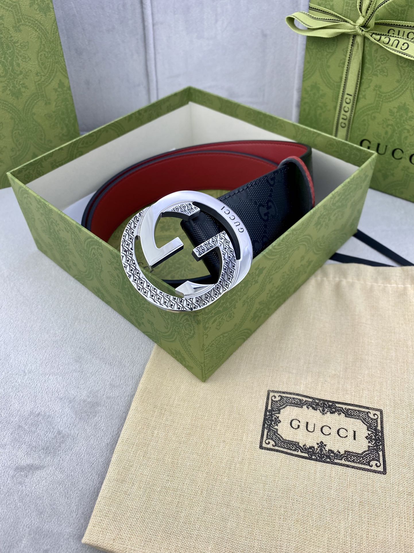 Gucci belt in green box with dark monogram strap, red trim, and silver buckle