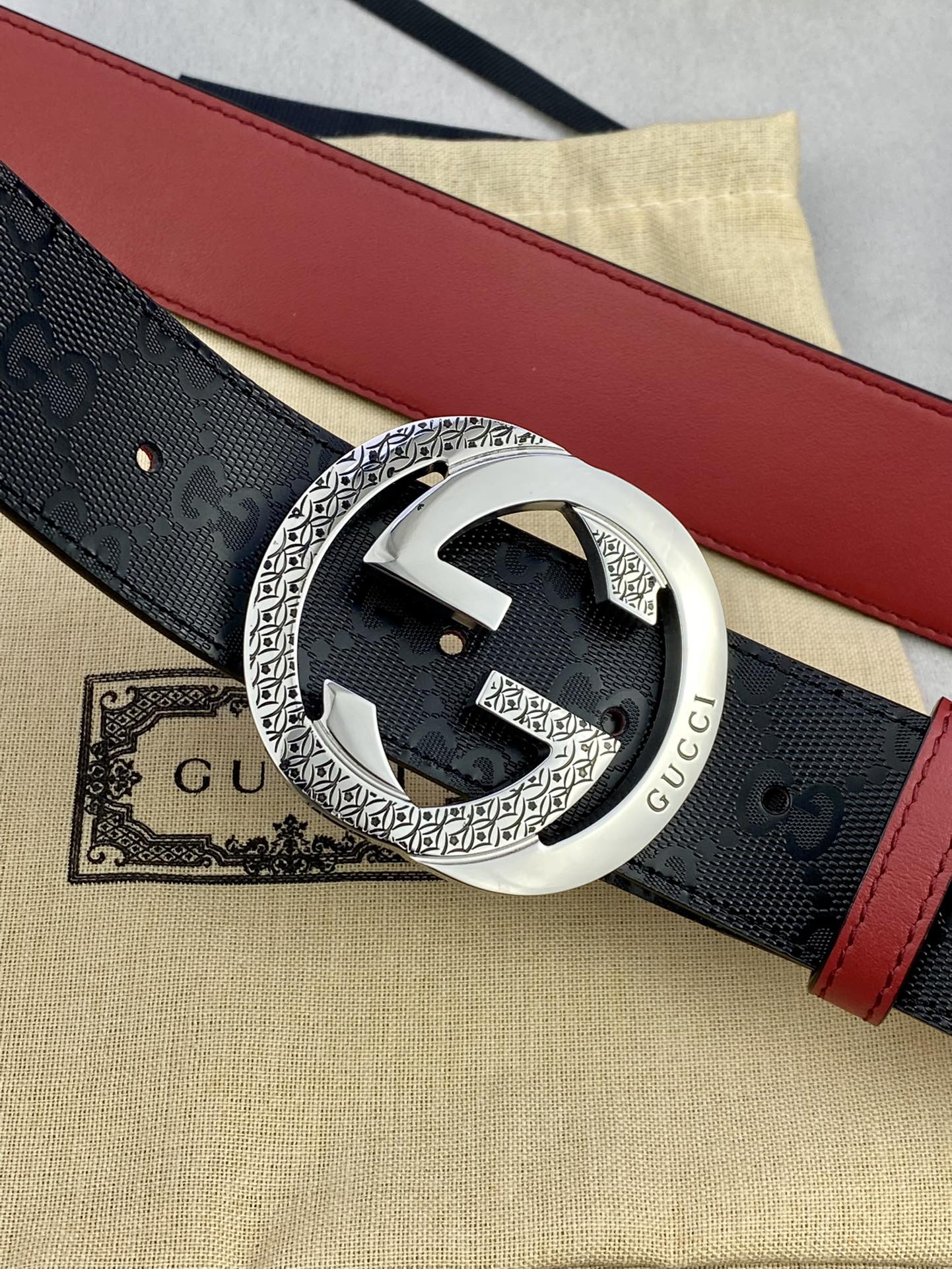 Gucci belt close-up with dark monogram strap, red edge, and silver buckle