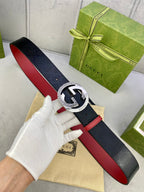 Gucci belt held in hand with dark leather, red trim, and silver double G buckle