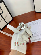 White leather belt with silver circular double-G buckle; strap with punched holes.