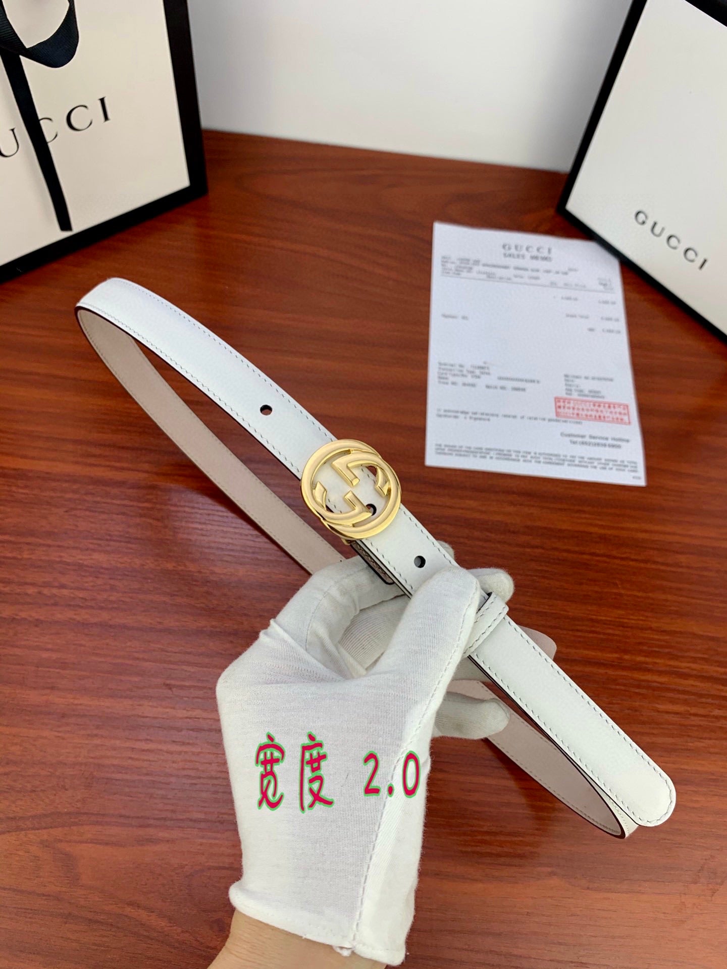 White leather Gucci belt with gold double-G buckle and stitched strap edge.