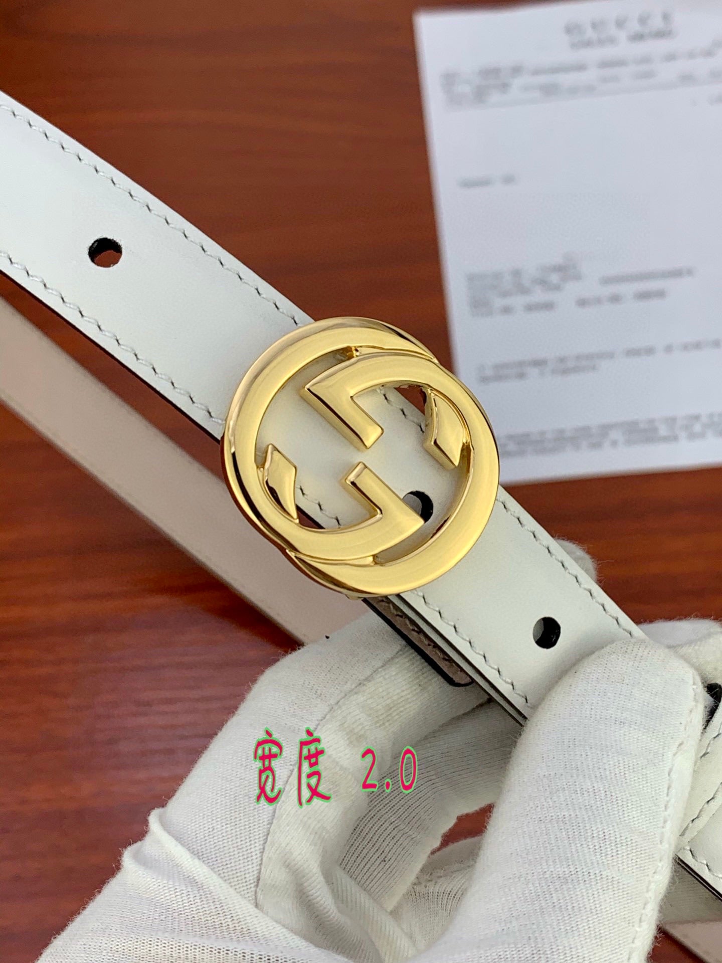 Close-up of white leather belt with gold double-G buckle and punched hole.