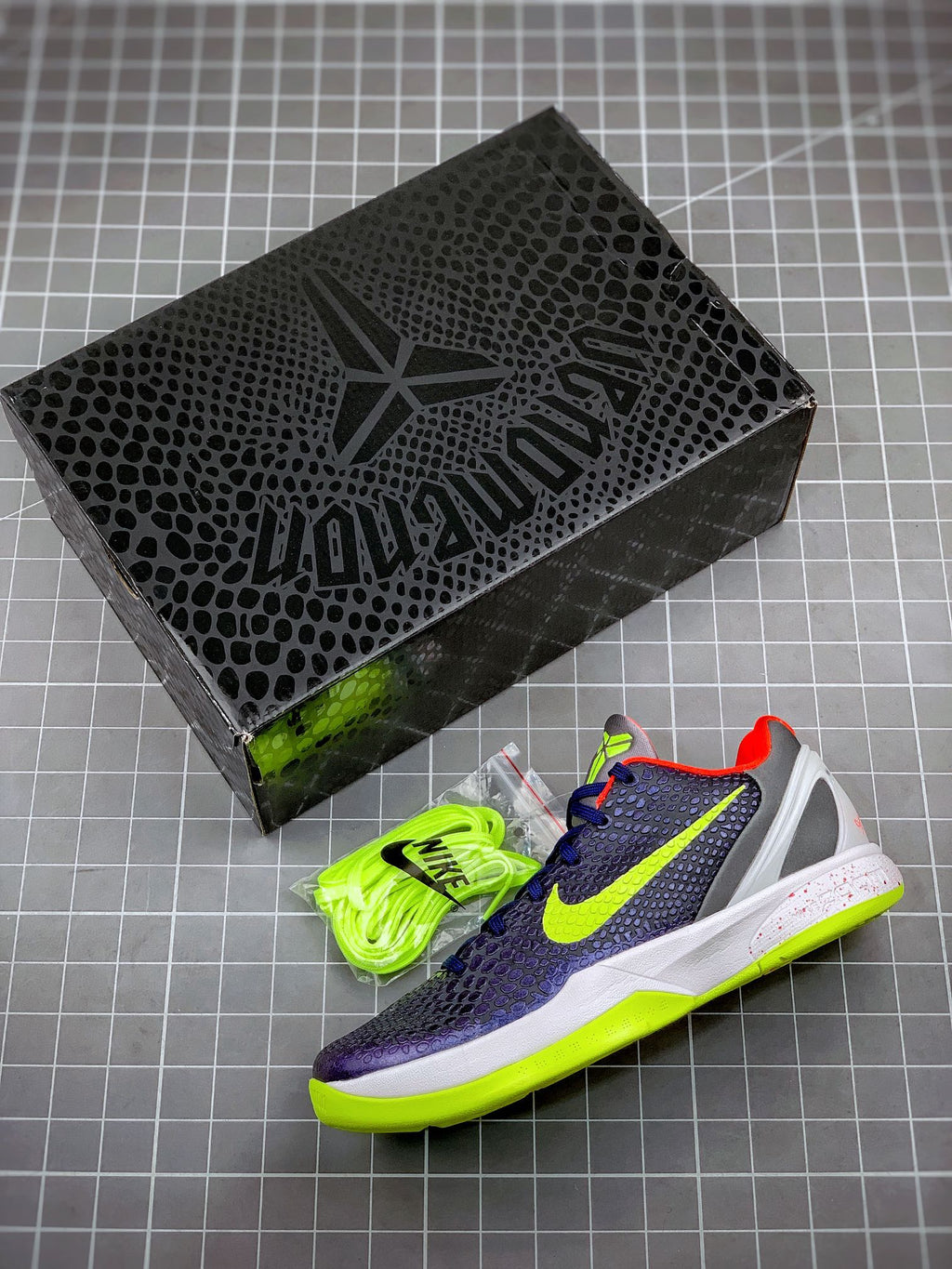 Pair of navy basketball sneakers with neon green accents and laces beside black box