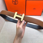 Brown leather belt with cream H buckle held flat for viewing