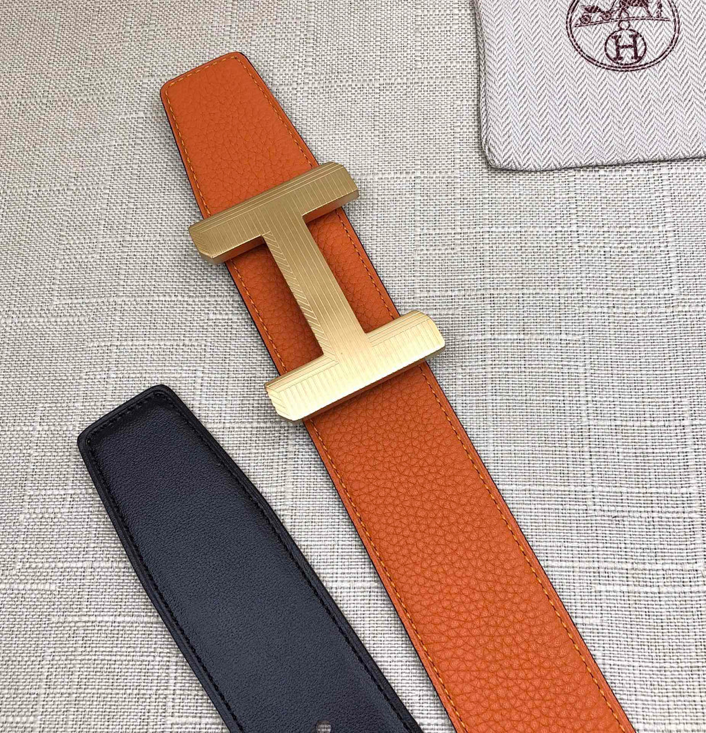 Hermes belt flat lay: orange leather strap with silver H buckle and black strap