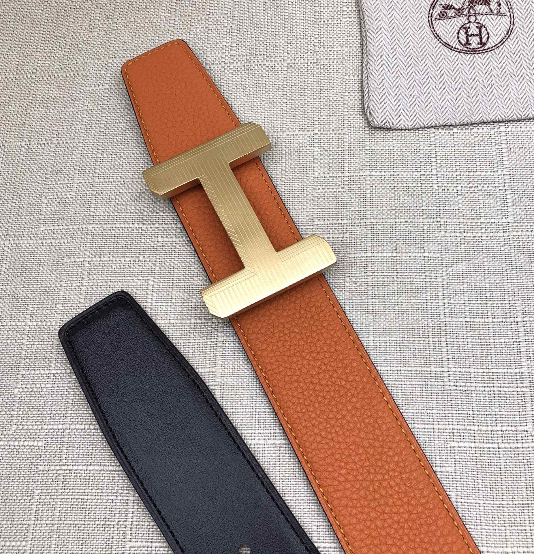 Hermes belt flat lay: orange leather strap with silver H buckle and black strap
