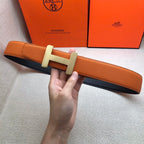Hermes belt held in hand: orange leather strap with silver H buckle and holes