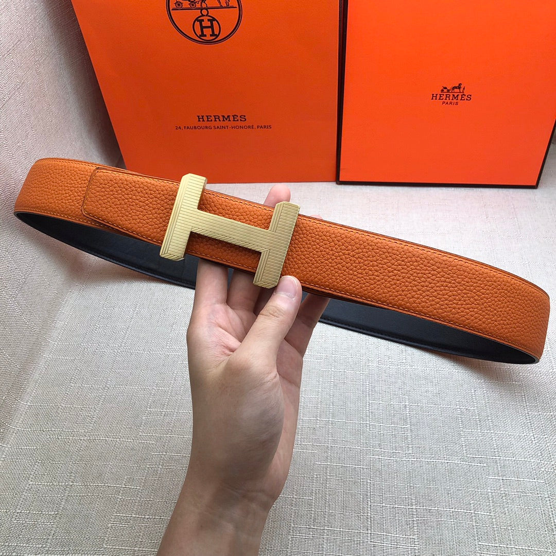 Hermes belt held in hand: orange leather strap with silver H buckle and holes