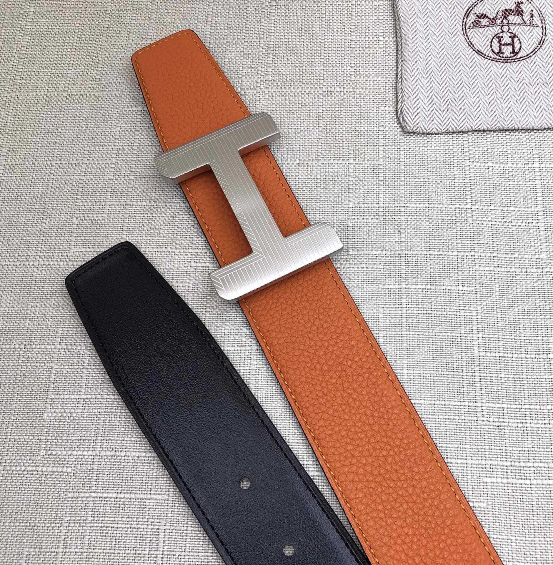 Hermes belt with orange leather strap and silver H buckle, black strap with holes