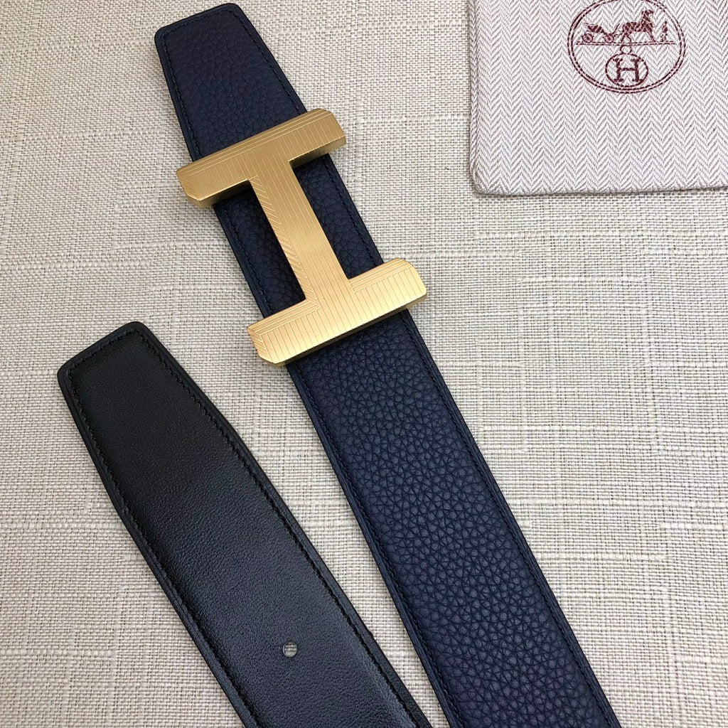 Navy leather belt with gold-tone H buckle; matching strap with two visible keeper holes.