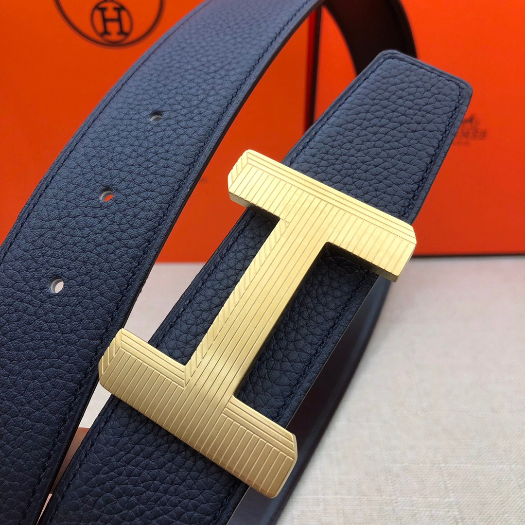 Leather belt detail: navy strap with gold-tone H buckle hardware and textured grain.