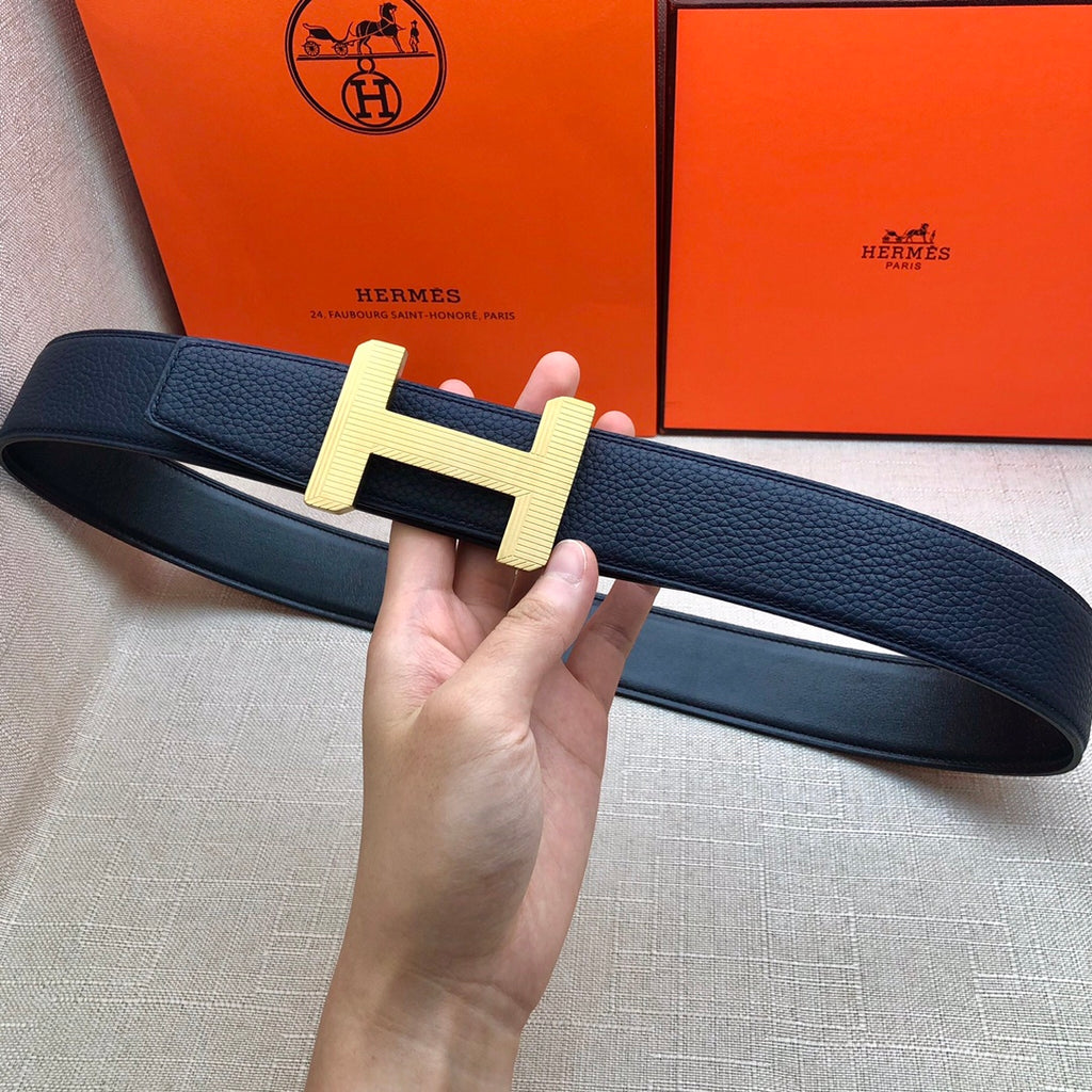 Leather belt held up: navy strap with gold-tone H buckle, smooth inner lining.