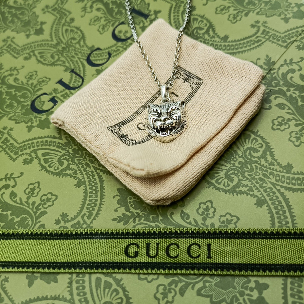Lion head pendant on silver chain over cream fabric pouch with logo patch