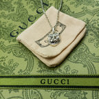 Lion head pendant on silver chain over cream fabric pouch with logo patch