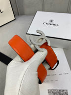 Designer belt with orange leather strap, rhinestone Chanel CC buckle, on white glove