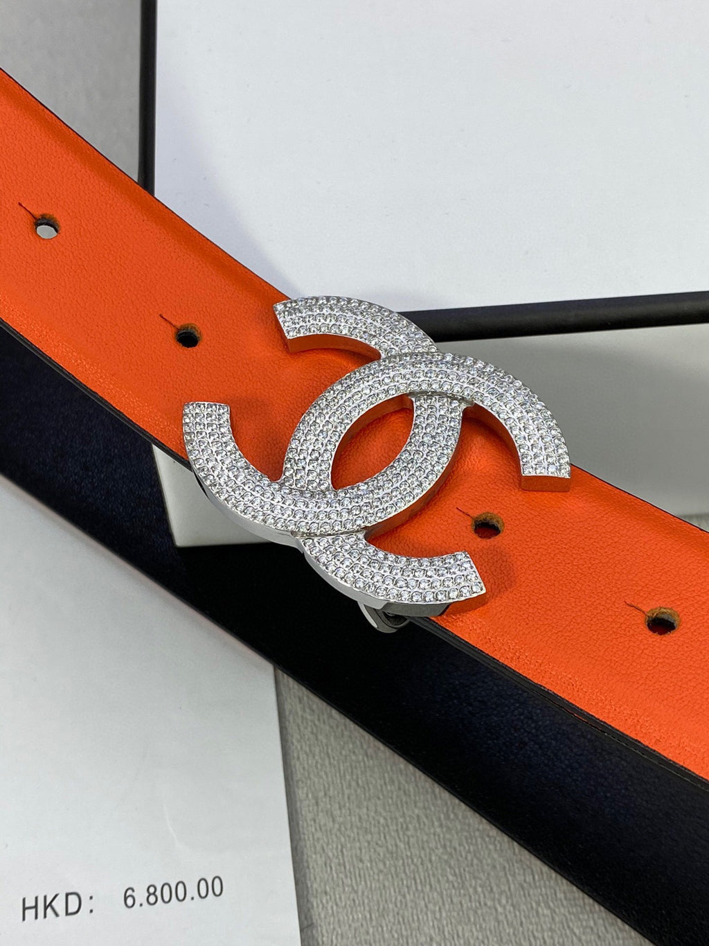 Designer belt with orange leather strap and rhinestone Chanel CC buckle, close-up
