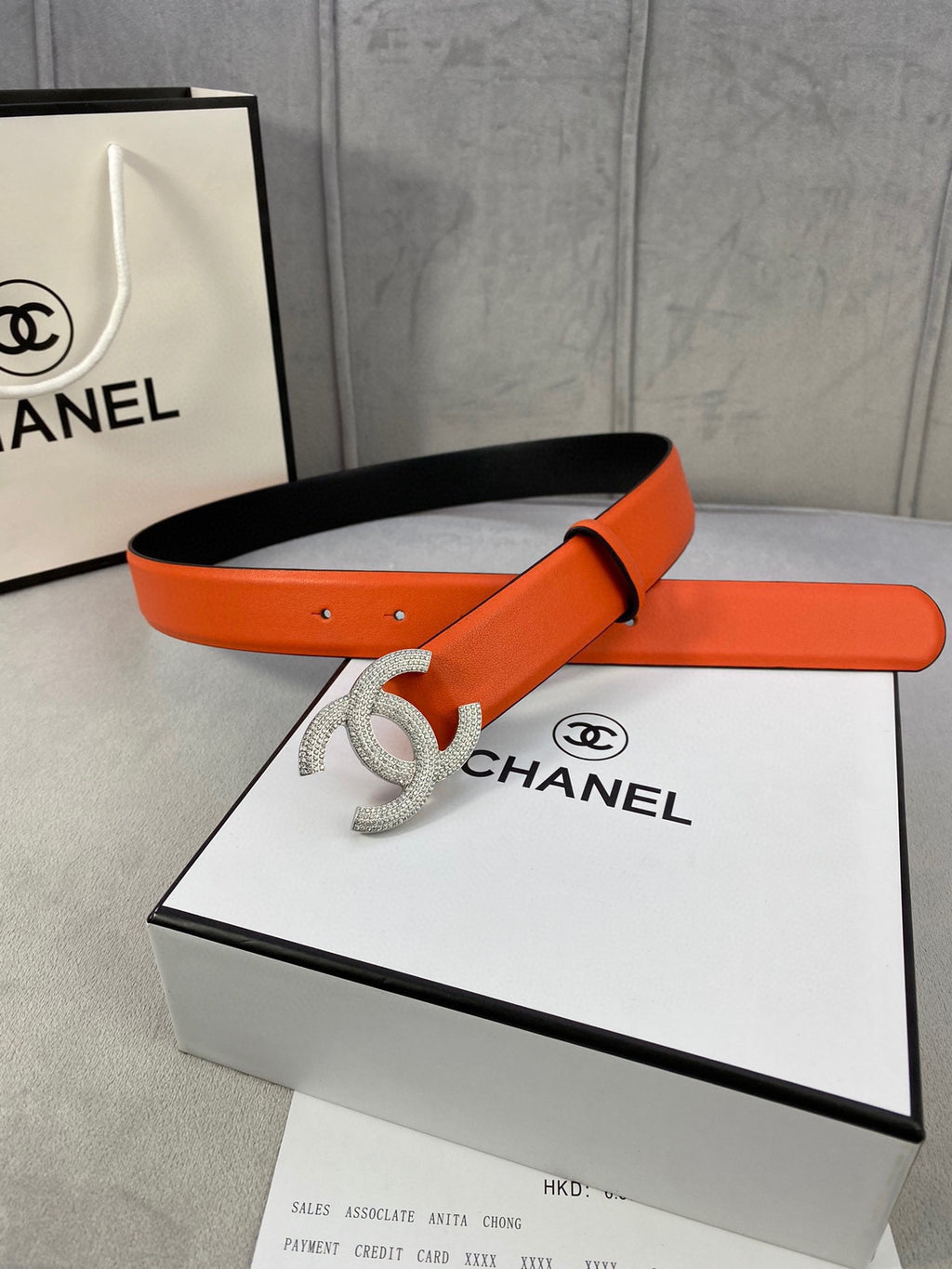 Designer belt with orange leather strap and rhinestone Chanel CC buckle, flat lay