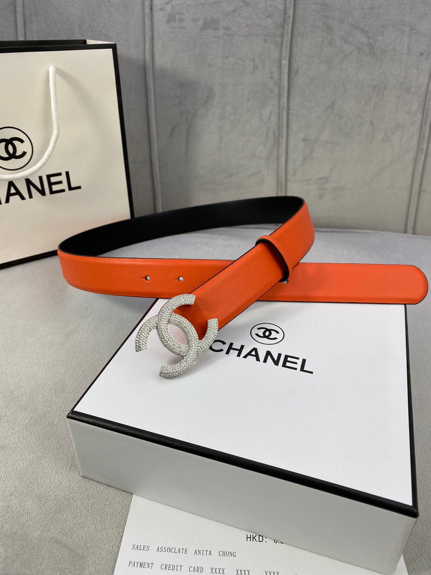 Designer belt with orange leather strap and rhinestone Chanel CC buckle, flat lay