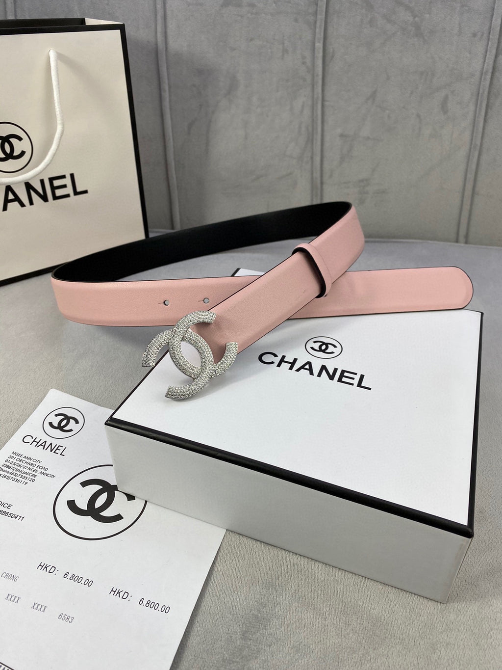 Chanel belt with light pink strap and rhinestone CC buckle, laid on boxes