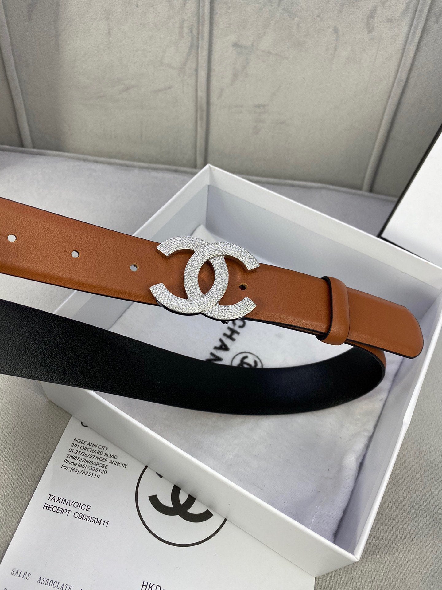 Tan leather belt with large rhinestone CC buckle on box packaging.