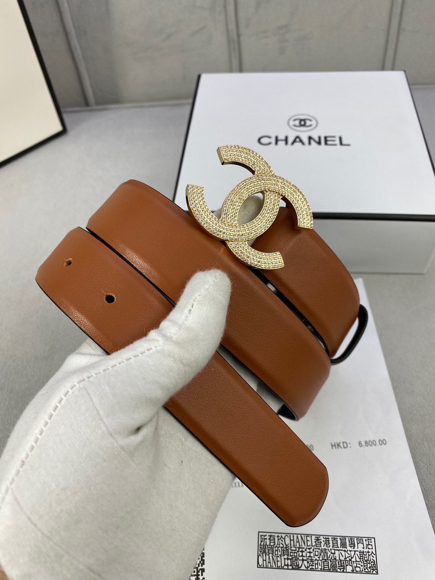 Tan leather belt with gold-tone rhinestone CC buckle, with protective white wrap.