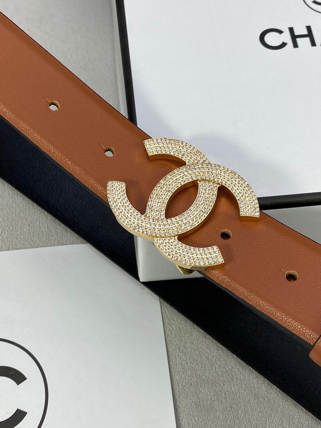Close-up of tan leather belt with gold-tone rhinestone CC buckle and punch holes.