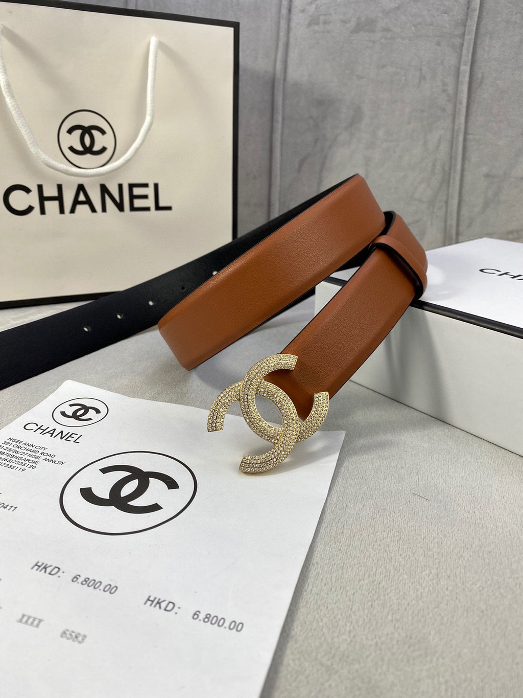 Tan leather belt with gold-tone rhinestone CC buckle, laid across Chanel bags.