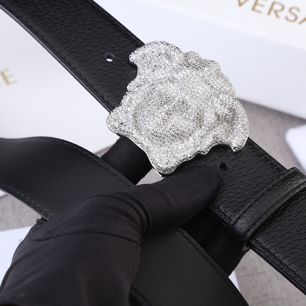 Black leather belt with gold-tone Medusa buckle close-up, textured surface.