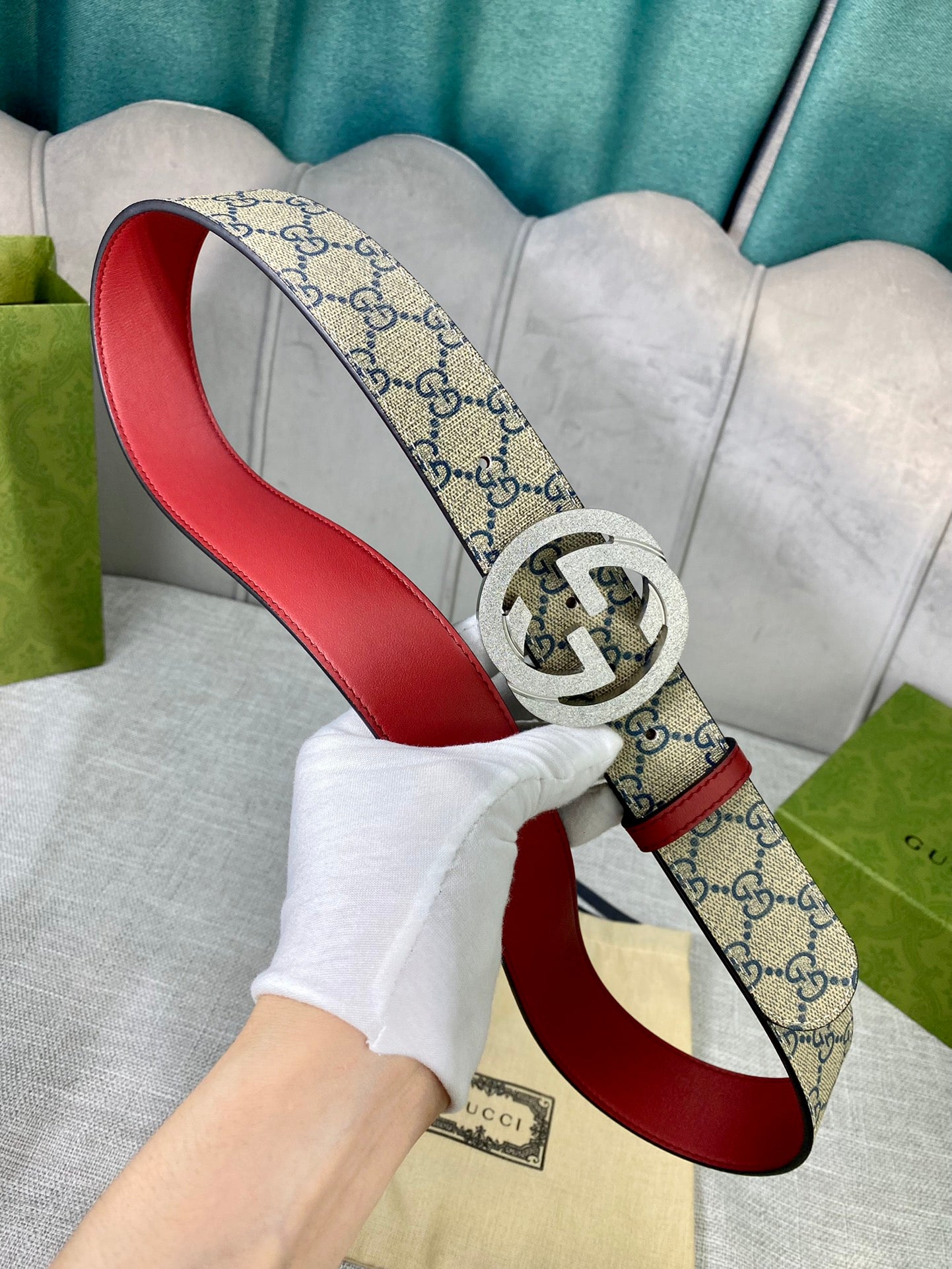 GG canvas belt with red leather trim and gold-toned interlocking buckle held in hand