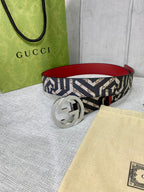 Logo-print belt with silver round G buckle, red leather lining, on a tabletop.