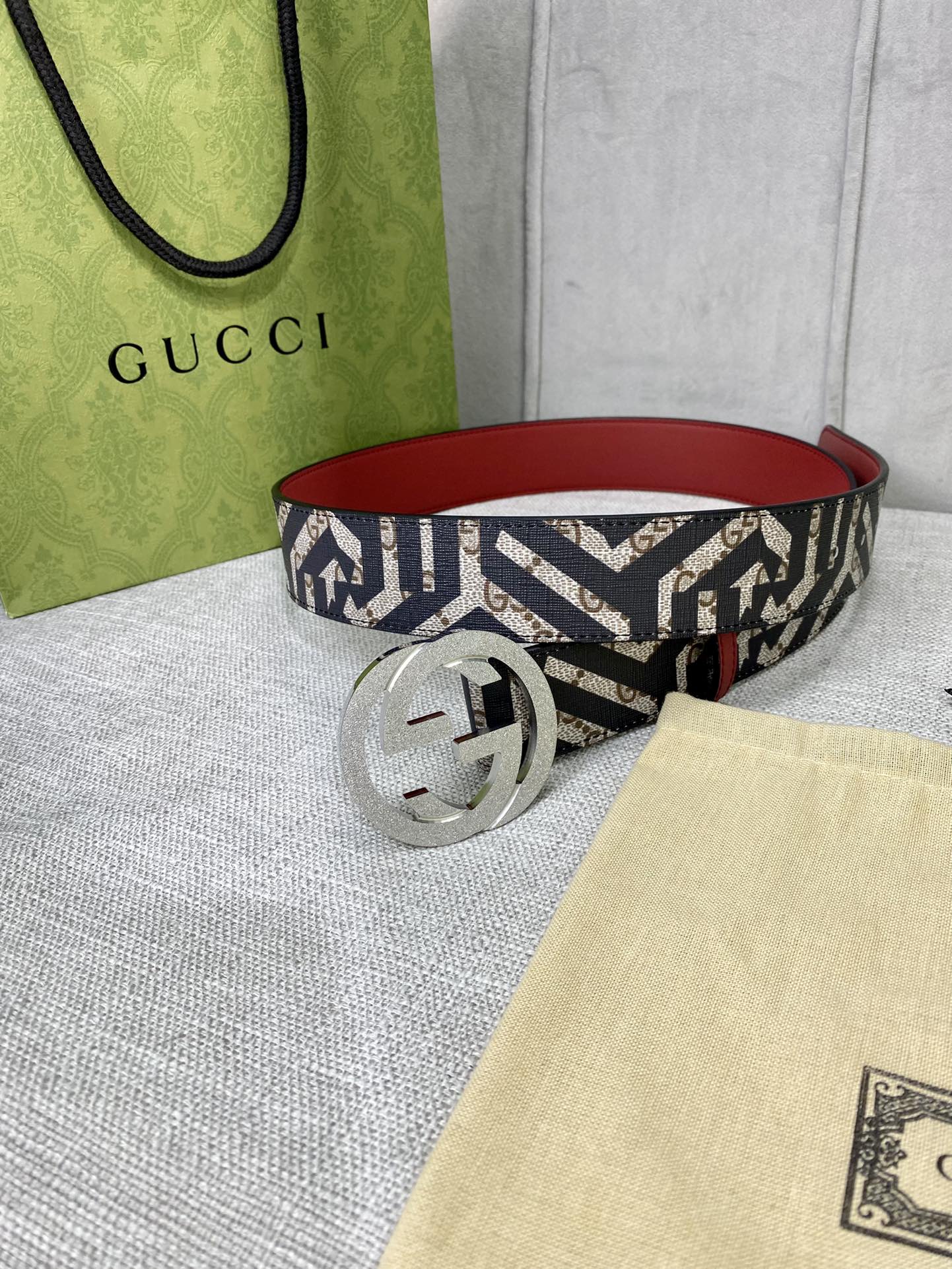 Logo-print belt with silver round G buckle, red leather lining, on a tabletop.
