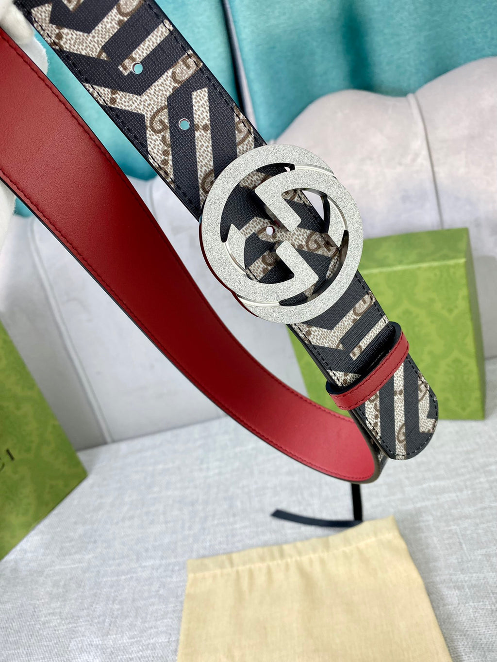 Logo-print belt with silver round buckle, red leather strap edge, held in gloved hand.