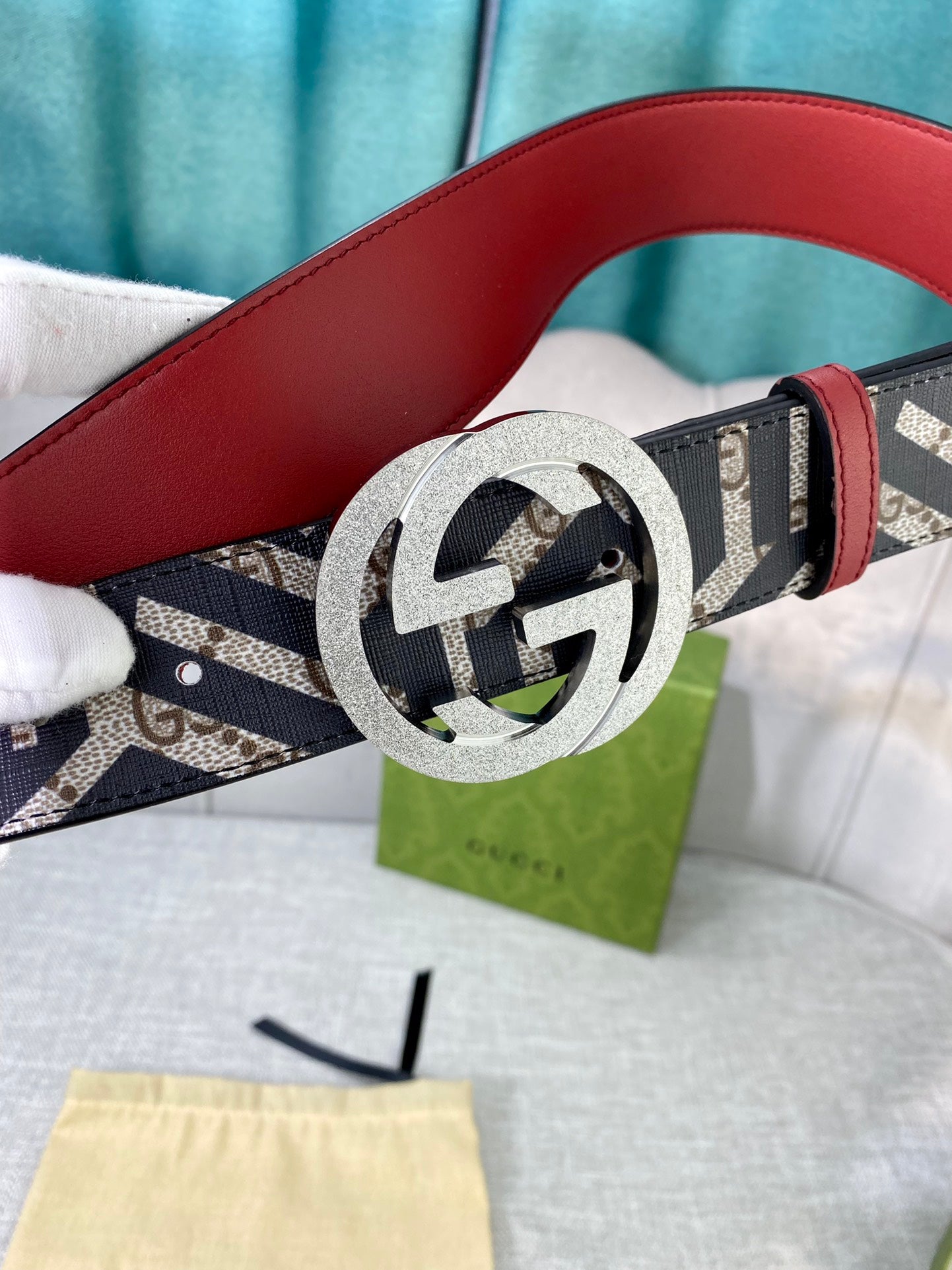 Logo-print belt with silver round buckle, red leather back strap, displayed on box.
