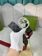 Designer belt shown at an angle: dark GG-print strap with red trim and silver-tone G buckle.