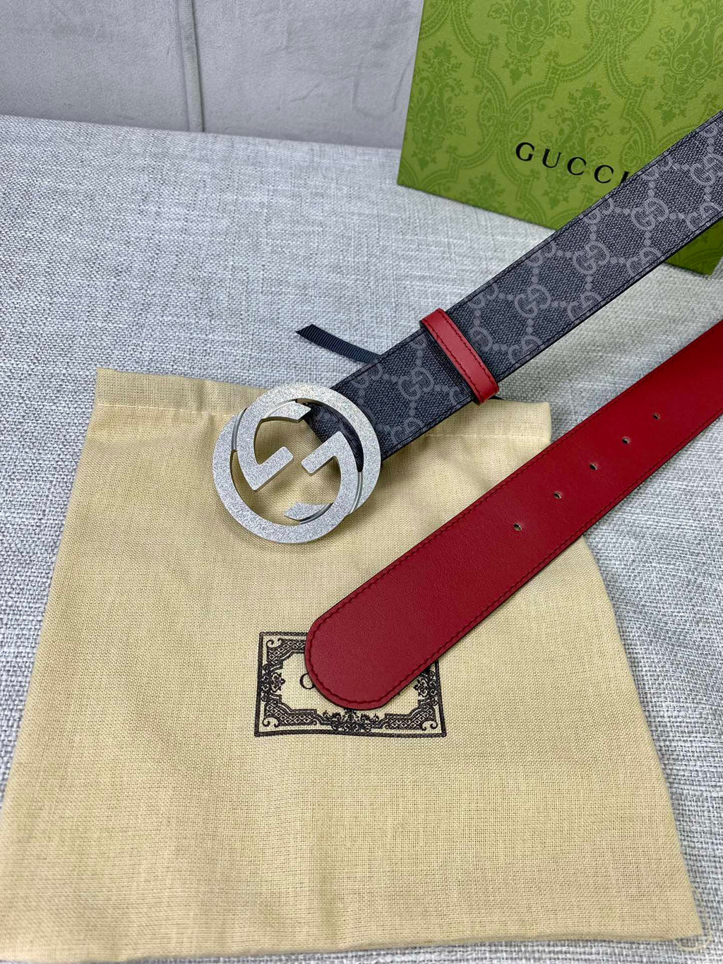 Designer belt flat on box: dark GG-print strap, red leather panel, gold-tone logo buckle.