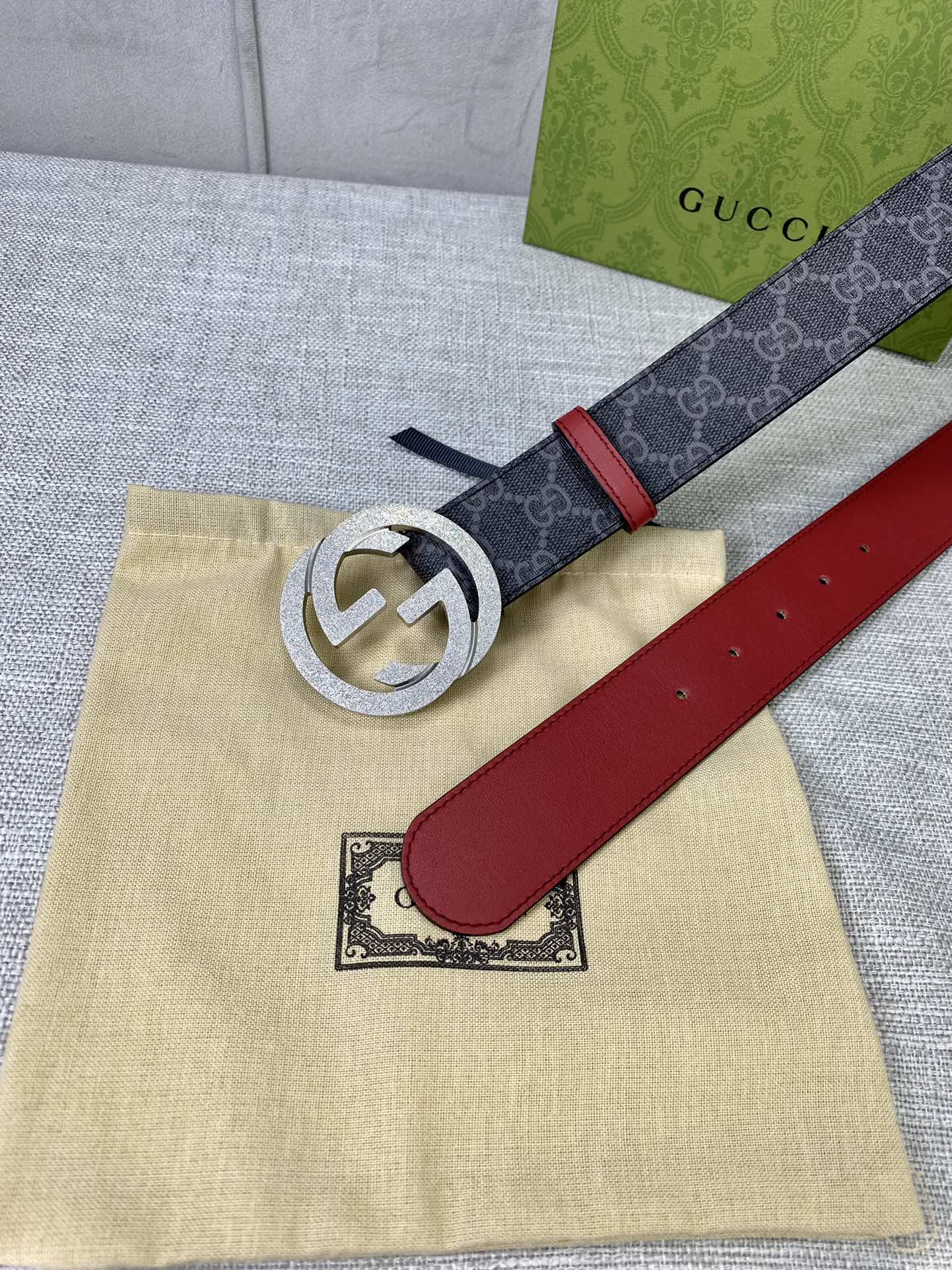 Designer belt flat on box: dark GG-print strap, red leather panel, gold-tone logo buckle.