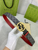 Designer belt held in hand: dark GG-print canvas with red leather strap and gold-tone buckle.