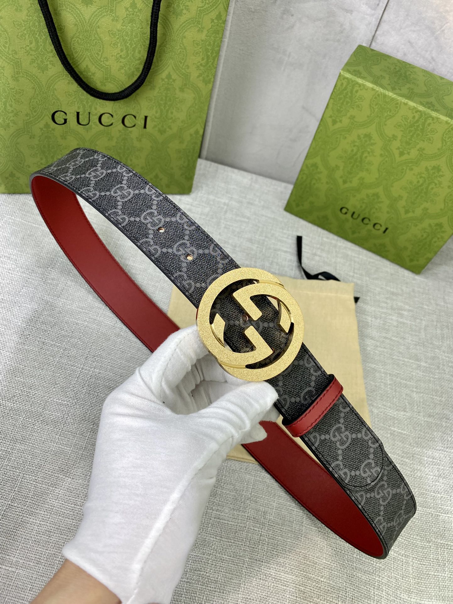 Designer belt held in hand: dark GG-print canvas with red leather strap and gold-tone buckle.