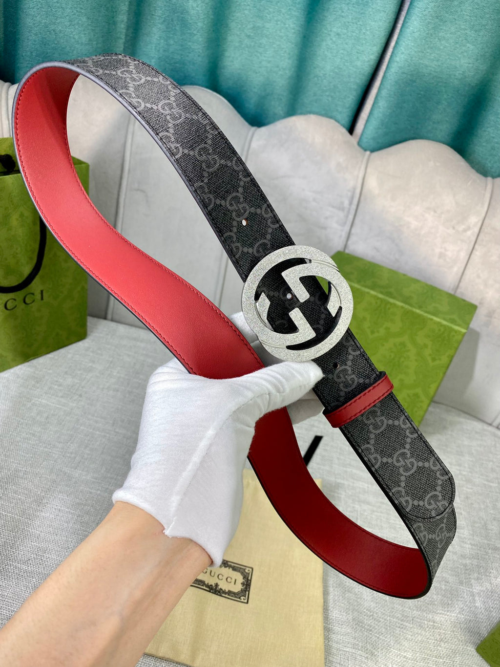 Designer belt detail with dark GG-print strap, red underside leather, and silver-tone logo buckle.