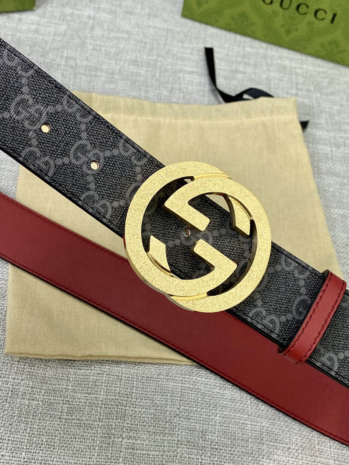 Designer belt close-up: dark GG-print strap with red leather side and gold-tone logo buckle.