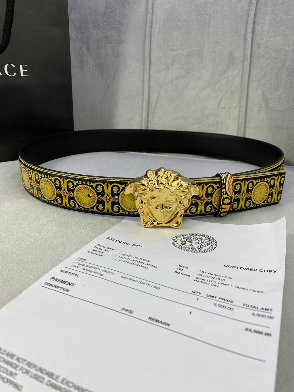 Designer belt lying flat: gold medallion trim with gold lion buckle on black strap