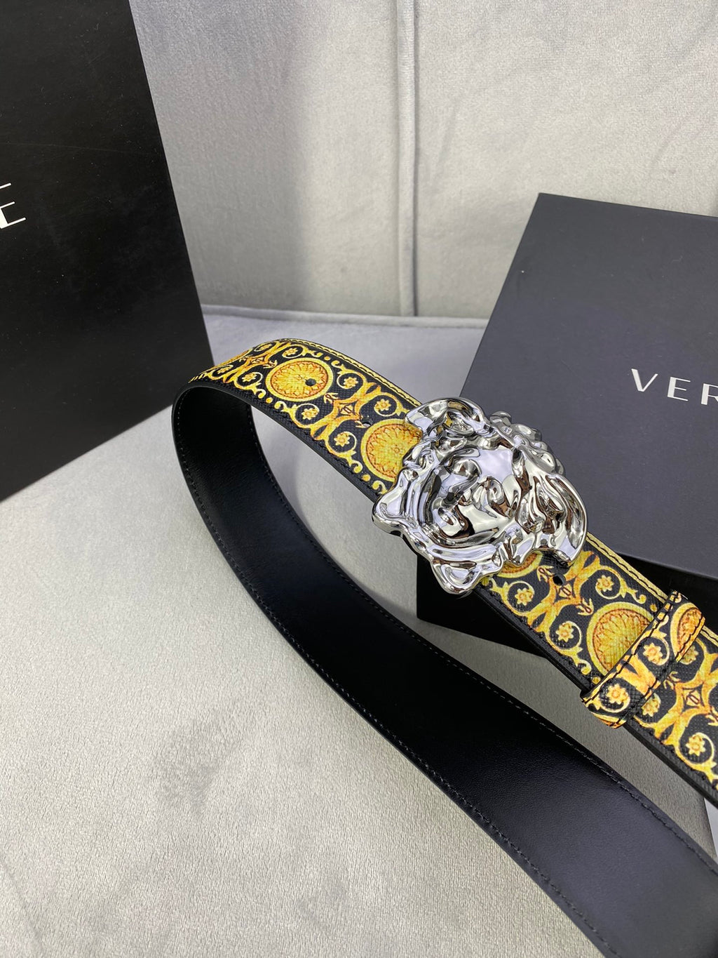 Designer belt angled view: black strap with gold medallion trim and silver lion buckle