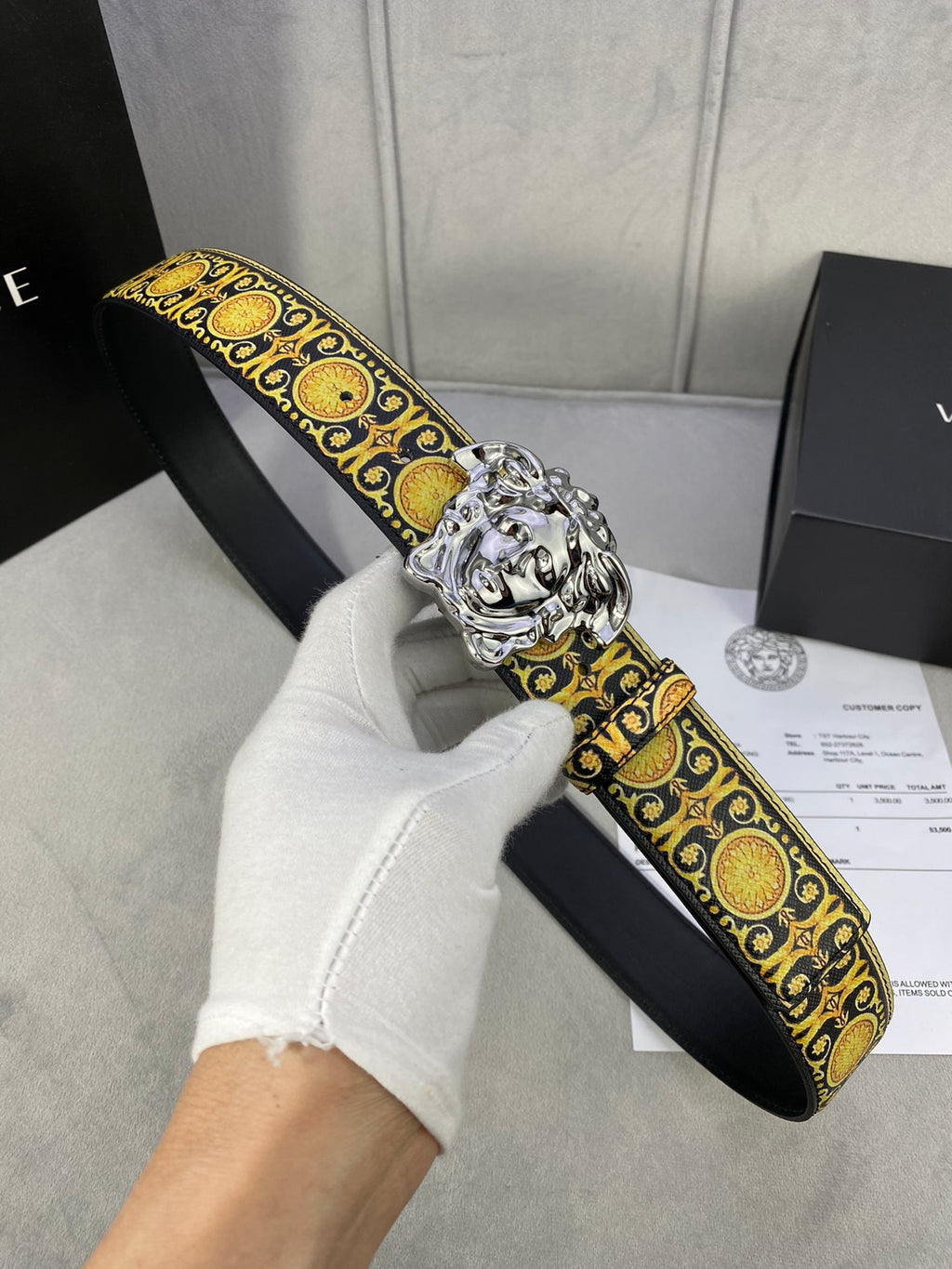 Designer belt with black strap, gold patterned trim, and large silver lion buckle