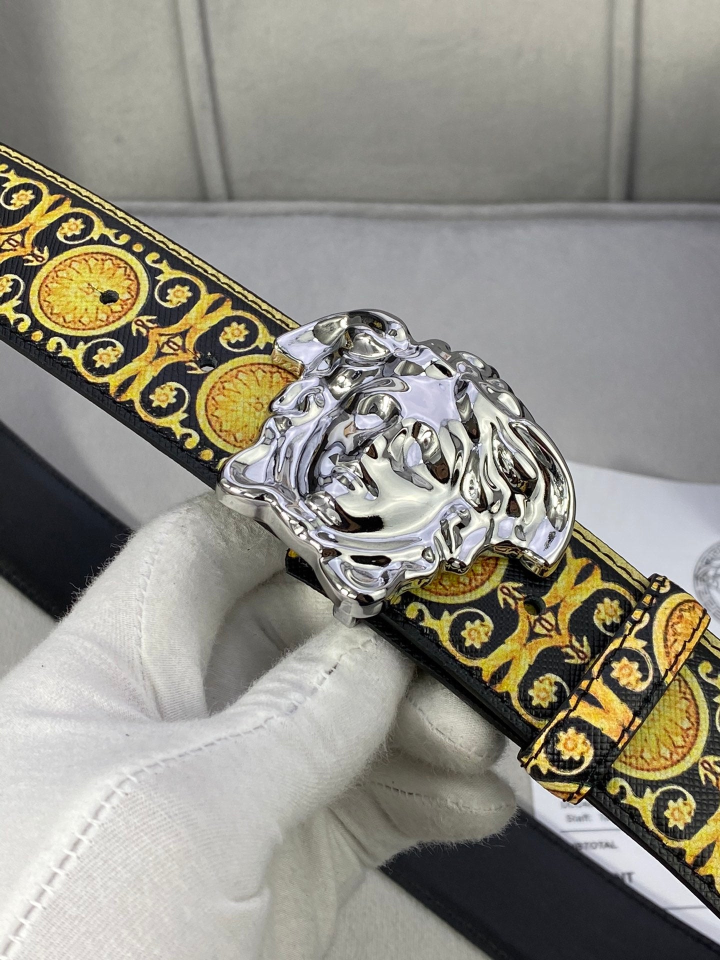 Designer belt close-up: black strap with gold medallion trim and silver lion buckle